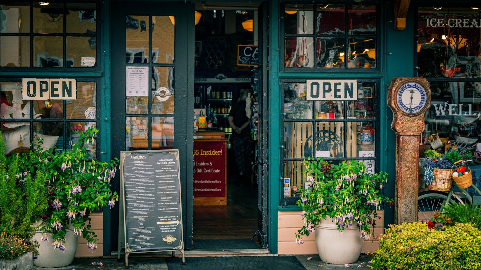 Storefront of a family-run general store with open signs and potted plants